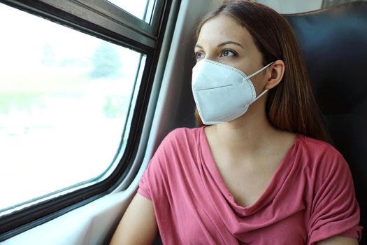 Travel safely on public transport. Young woman with KN95 FFP2 face mask looking through train window. Train passenger with protective mask.
