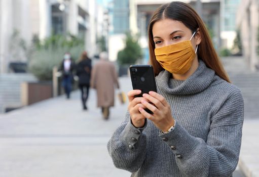 Portrait of young woman with face mask sitting outside as lockdown opens holding smartphone