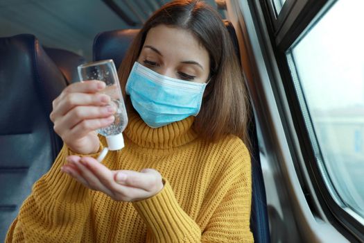 Travel safely on public transport. Young woman with surgical mask using hand sanitizer gel from dispenser. Commuter with protective mask disinfects hands with alcohol gel on public transport.