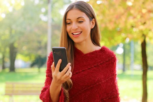 Beautiful woman with red poncho reading sms on her mobile phone outdoor.