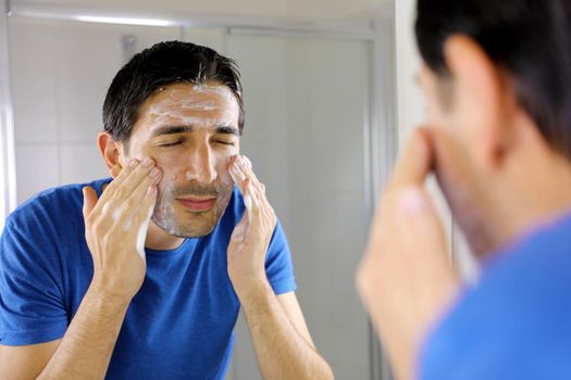 Man washing face with facial cleanser face wash soap in bathroom at home. Men skin care concept.
