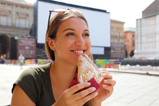 Young woman having italian breakfast with croissant and coffee at the cafe on the street in summertime
