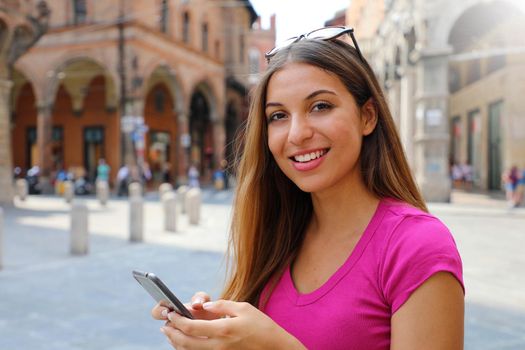 Portrait of smiling woman looking at camera and using smart phone in old medieval town