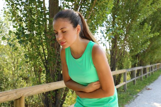 Woman has side cramp. Young woman suffering from abdominal pain while running outdoor.