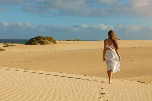 Amazing view of young woman walking barefoot on desert dunes at sunset in Corralejo, Fuerteventura