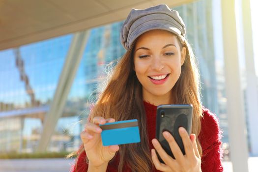 Portrait of a happy shopper girl paying on line with credit card outdoor.