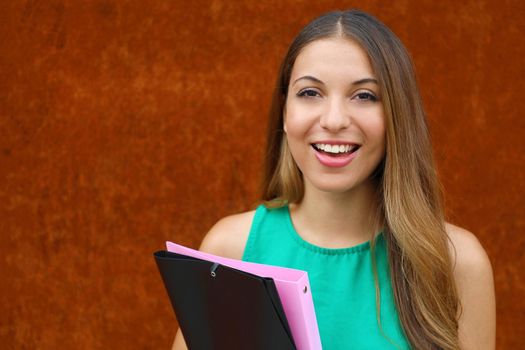 Close up young business woman holding folders outdoor on rust background with copy space.