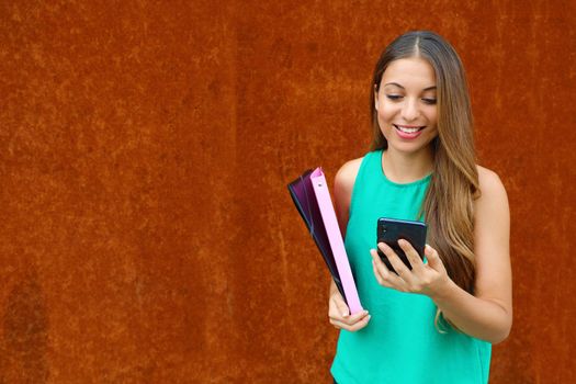 Young business woman typing on smart phone with rust background and copy space.