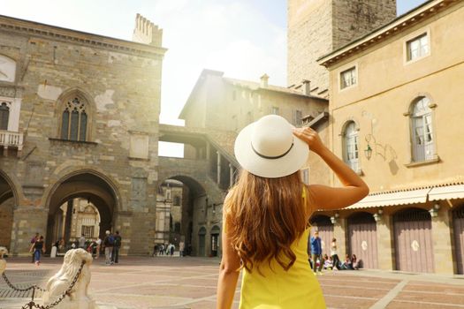 Beautiful girl with hat visiting Piazza Vecchia square in Bergamo Citta Alta medieval old city of Lombardy region in Italy.