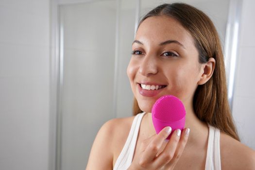 Close up of smiling girl cleaning skin with silicon brush ultrasonic in the bathroom