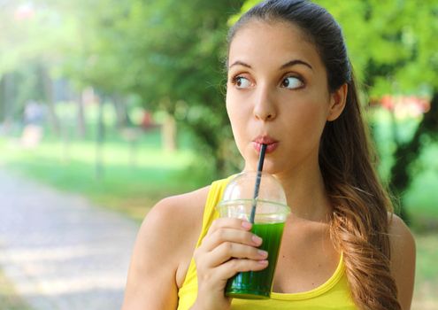 Young beautiful sporty woman drinking green detox smoothie. Fitness girl drinking vegetable smoothie after fitness running workout on summer day.