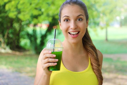 Young beautiful sporty woman drinking green detox smoothie. Fitness girl drinking vegetable smoothie after fitness running workout on summer day.