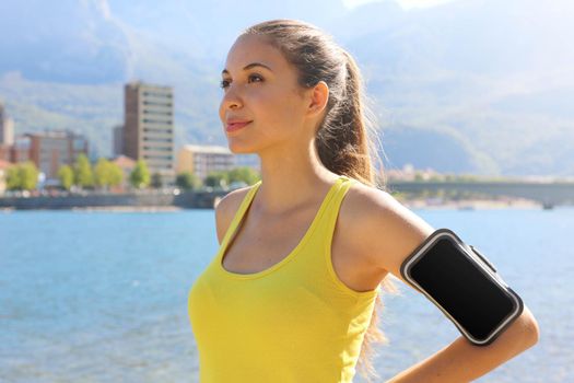 Successful positive female athlete wearing armband blank for advertising before running or exercising outdoor in summer. Woman success in sport lifestyle.
