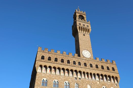Palazzo Vecchio city hall palace on Piazza Della Signoria square in Florence, Italy. Famous historical building with bell tower with clock on blue sky background. 