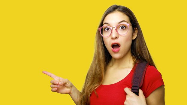Astonished student pointing finger copy space over yellow background