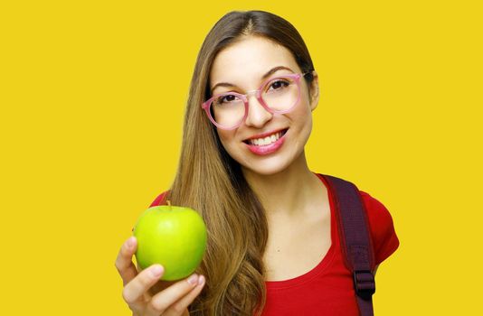 Portrait of a smiling nerd happy girl with glasses and green apple in her hand isolated over yellow background