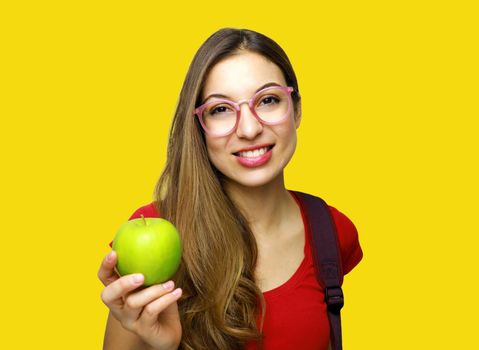 Portrait of a smiling nerd happy girl with glasses and green apple in her hand isolated over yellow background