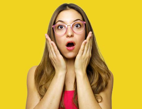Close-up portrait of surprised beautiful girl holding her head in amazement and open-mouthed. Over yellow background.