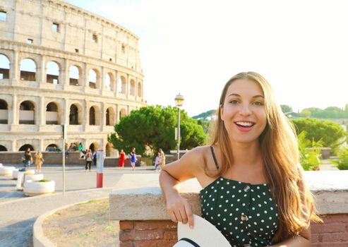 Happy smiling beautiful tourist girl in Rome with Colosseum on the background at sunset. Summer holidays in Italy.
