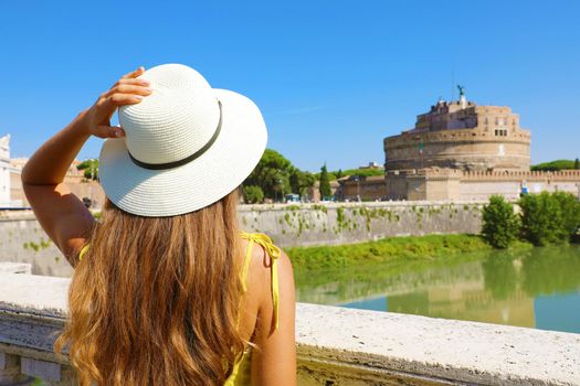 Holidays in Italy. Back view of beautiful tourist girl in Rome, Italy. Attractive fashion woman looks at Castel Sant Angelo castle on the bridge.