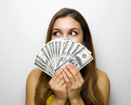 Portrait of successful woman covering mouth with fan of 100 dollar bills looking to the side being satisfied about salary or income over white background 