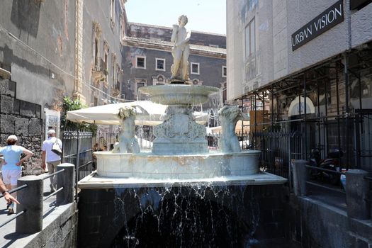 CATANIA, SICILY - JUNE 19, 2019: Amenano fountain and marble sculptures over the underground river running under Catania city centre in Sicily, Italy