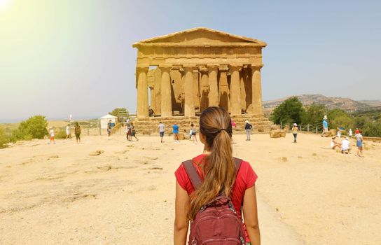 Young woman looks at Concordia Temple in the Valley of the Temples of Agrigento, Sicily. Traveler girl visits Greek Temples in Southern Italy formerly Magna Graecia.