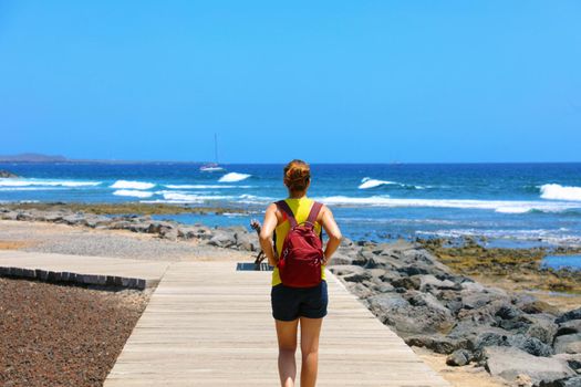 Female hiker walking on catwalk  with spectacular landscape of Playa de Las Americas beach, Tenerife, Spain