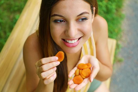 Brazilian girl eating dried apricots outdoors looking to the side. Healthy food concept.