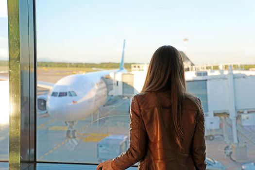 Young woman in the airport looking through the window at airplanes