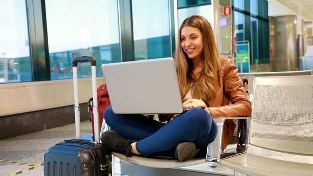 Young traveler woman using laptop at the airport sitting with crossed legs
