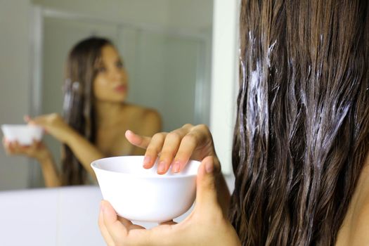 Hair masking. Young woman hand applying natural mask on long healthy hair. Health and beauty concept.