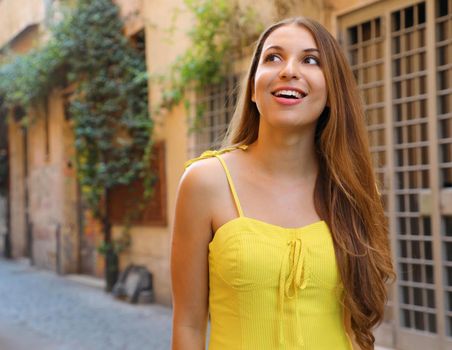 Portrait of beautiful girl with long hair in yellow summer dress walking in Trastevere neighborhood Rome, Italy.