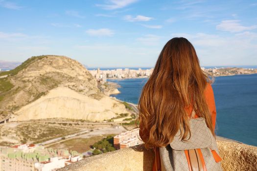 Back view of traveler girl enjoying view of Alicante city from Santa Barbara castle, Spain. Young female backpacker relaxing in her travel in southern Europe.