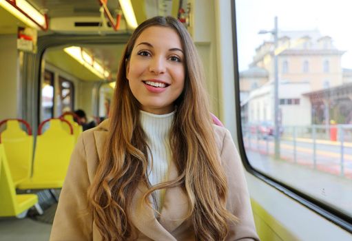 Young woman in sweater and coat sitting in the tram smile at camera.