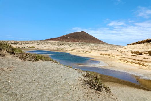 Amazing view of Montana Roja volcano with pond in natural reserve of sand desert of El Medano, Tenerife, Spain