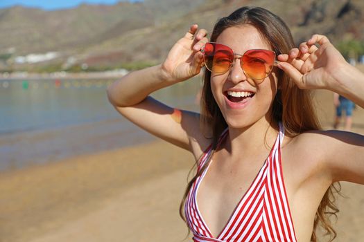 Happy playful bikini girl with sunglasses on the beach