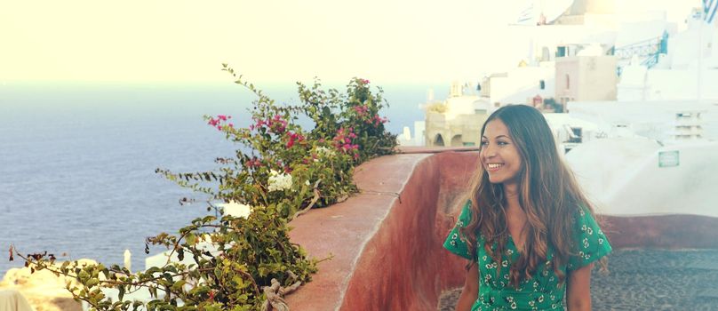 Happy smiling fashion girl with green dress walking in Oia village, Santorini. Excited female travel tourist on her summer vacations in Greece. Banner panoramic crop.