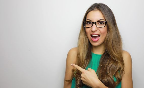 Portrait of happy woman in glasses pointing finger away at copyspace isolated on a white background