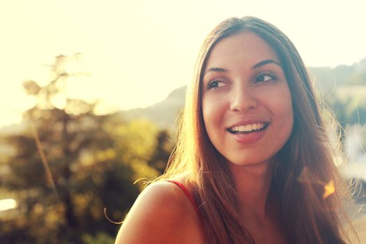 Portrait of happy smiling woman standing on sunny summer or spring day outside. Cute smiling woman looking to the side filtered image, flare sunshine.