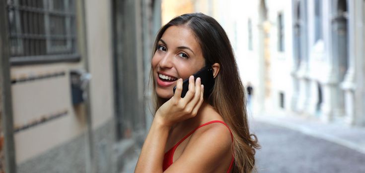 Attractive brunette businesswoman talking on mobile phone with client outdoor. Banner crop panorama.