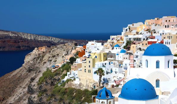 Stunning panoramic view of Santorini island with white houses and blue domes on famous Greek resort Oia, Greece, Europe. Traveling concept background. 
