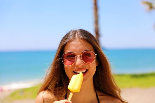 Beautiful girl looking to the side with sunglasses eating popsicle on Malaga beach in her travel holidays in Southern Spain