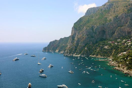 Spectacular view of Capri rocky coast with yatchs and luxury ships in blue turquoise sea, Capri Island, Campania, Italy