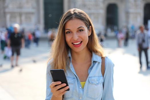 Attractive casual woman wearing shirt texting on the smart phone and looking at camera
