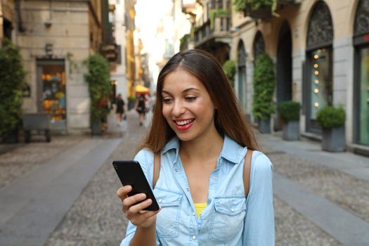 Beautiful young woman messaging on the smart phone with Milan city street in background. Pretty girl having smart phone conversation.