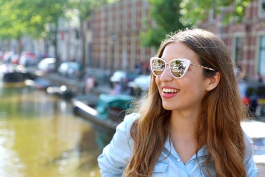 Portrait of beautiful cheerful girl with sunglasses looking to the side on one of typical Amsterdam channels, Netherlands, Europe