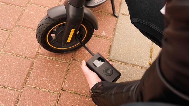 A man pumps air into the wheel of an electric scooter using a special device.