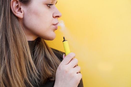 A young girl smokes disposable electronic cigarette. Bright yellow background