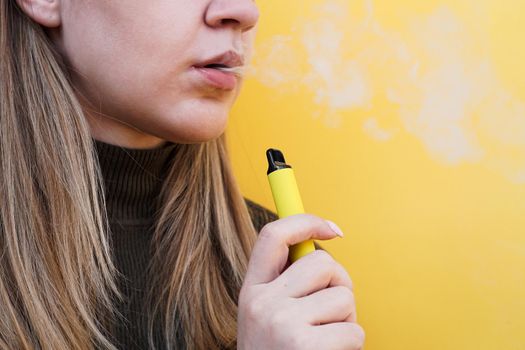 A young girl smokes disposable electronic cigarette. Bright yellow background